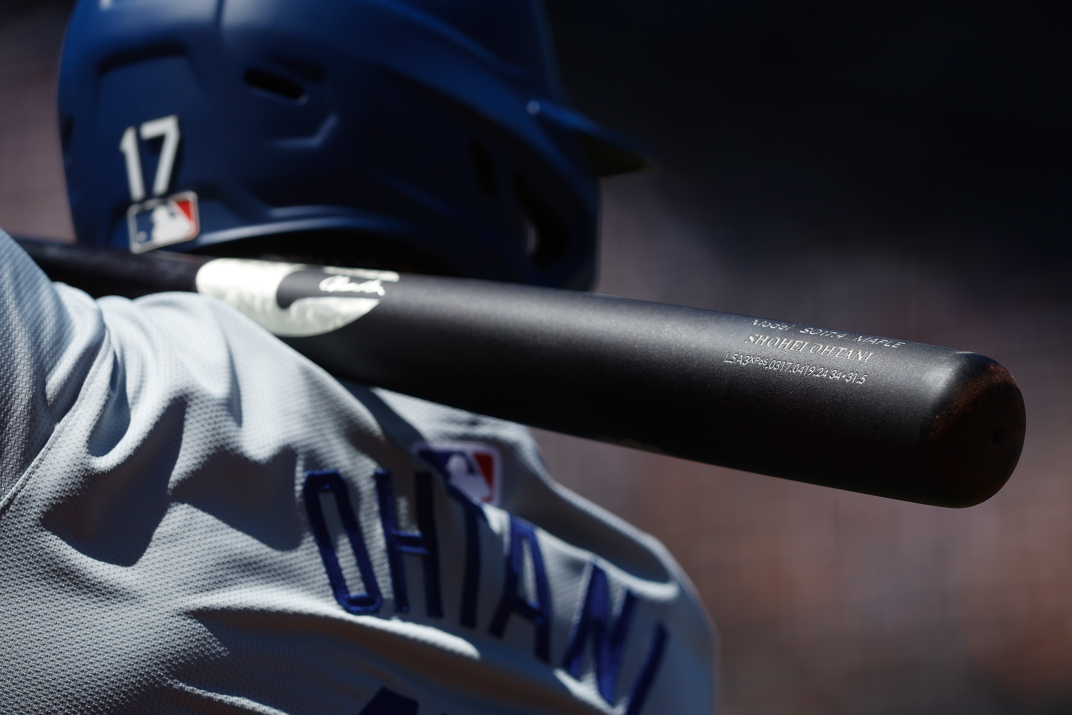 A close up shot of Ohtani from behind, primarily featuring his jersey’s nameplate, his bat, and the back of his helmet featuring the number 17