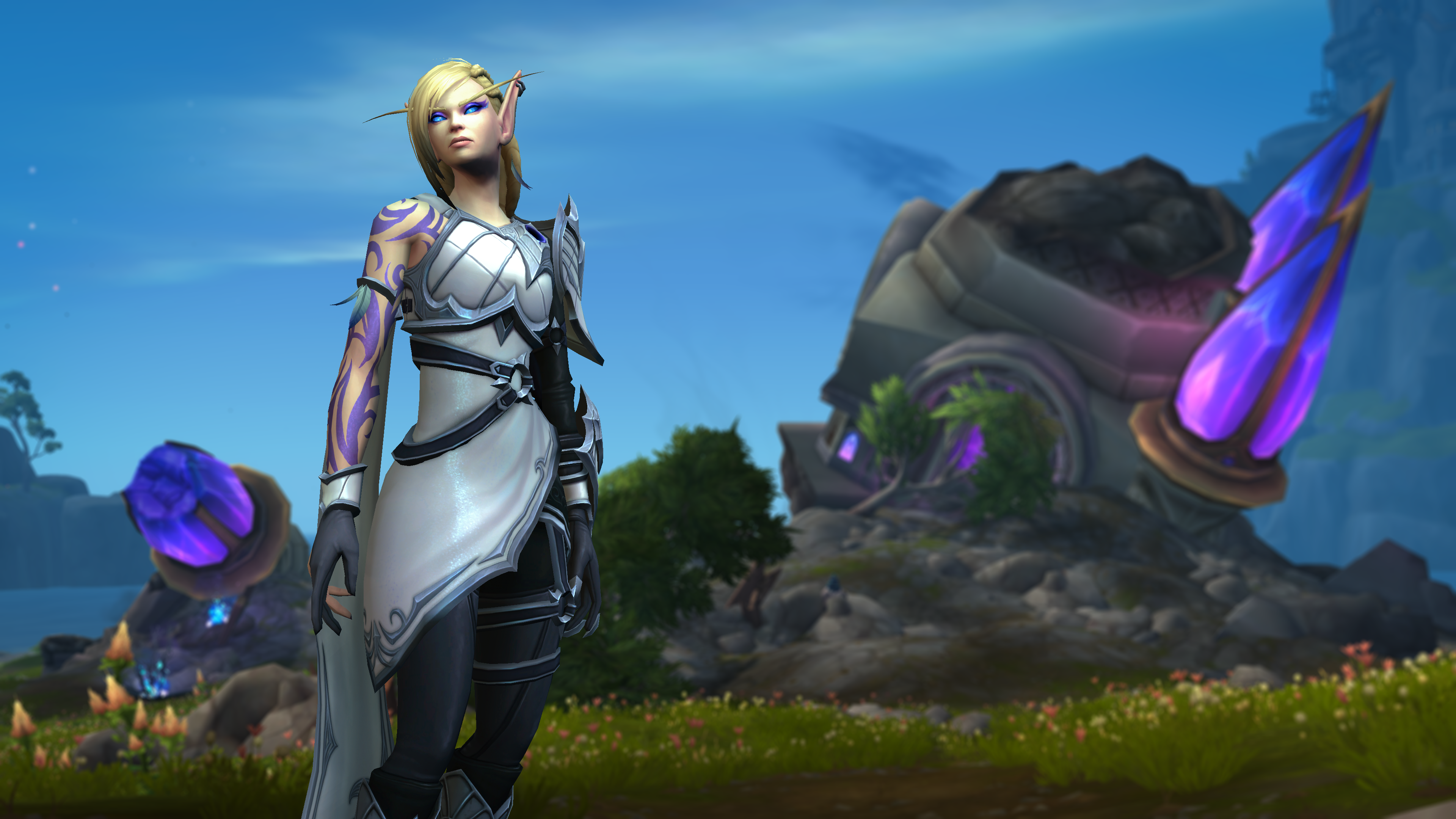 Alleria Windrunner, an elf with short blond hair and a contemplative expression, dressed in white garb with purple tattoos running down one arm, stands in front of a crumbled structure marked with big purple crystals.