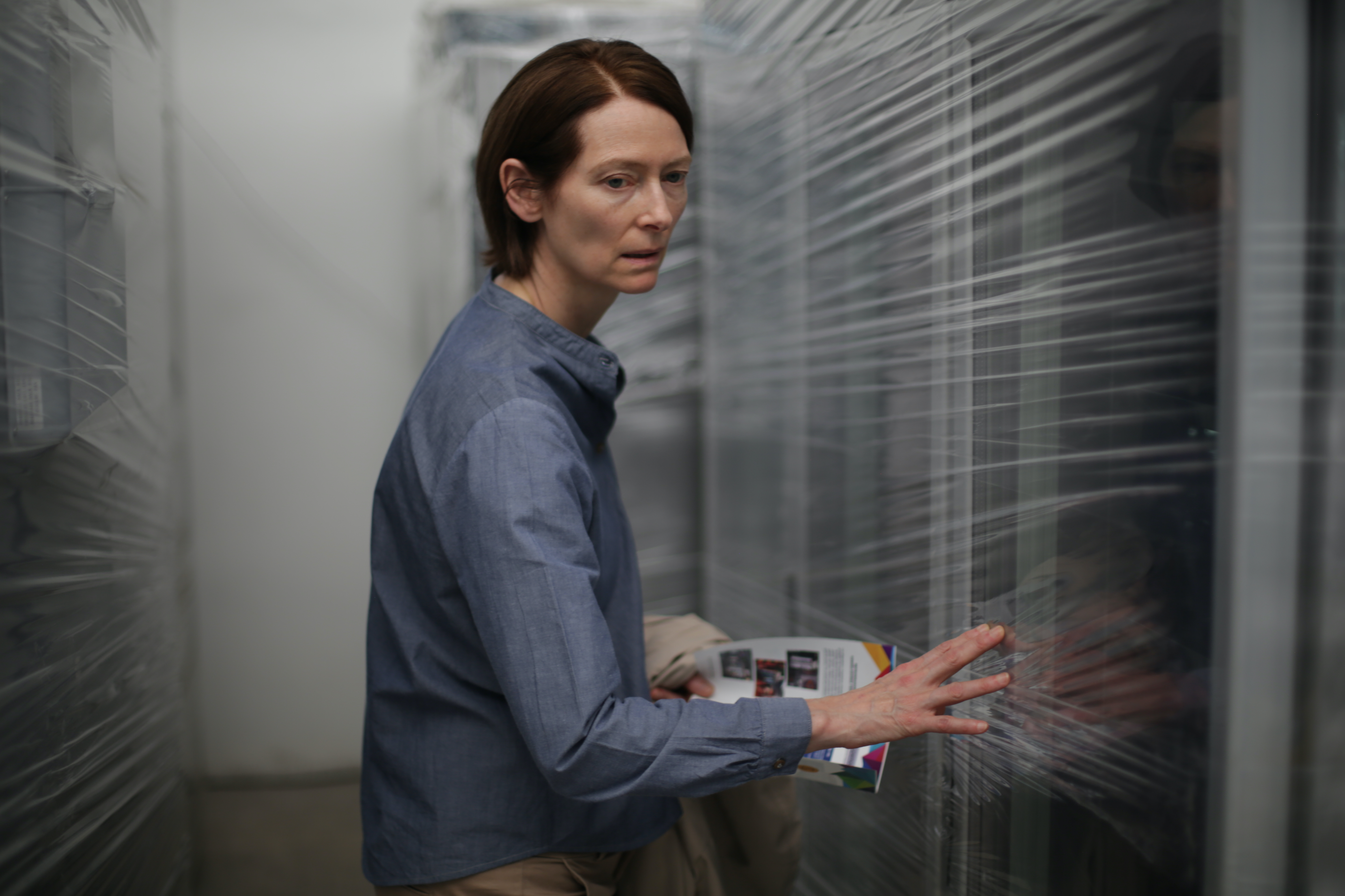 Tilda Swinton looking confused against a blurred background of white slats in Memoria