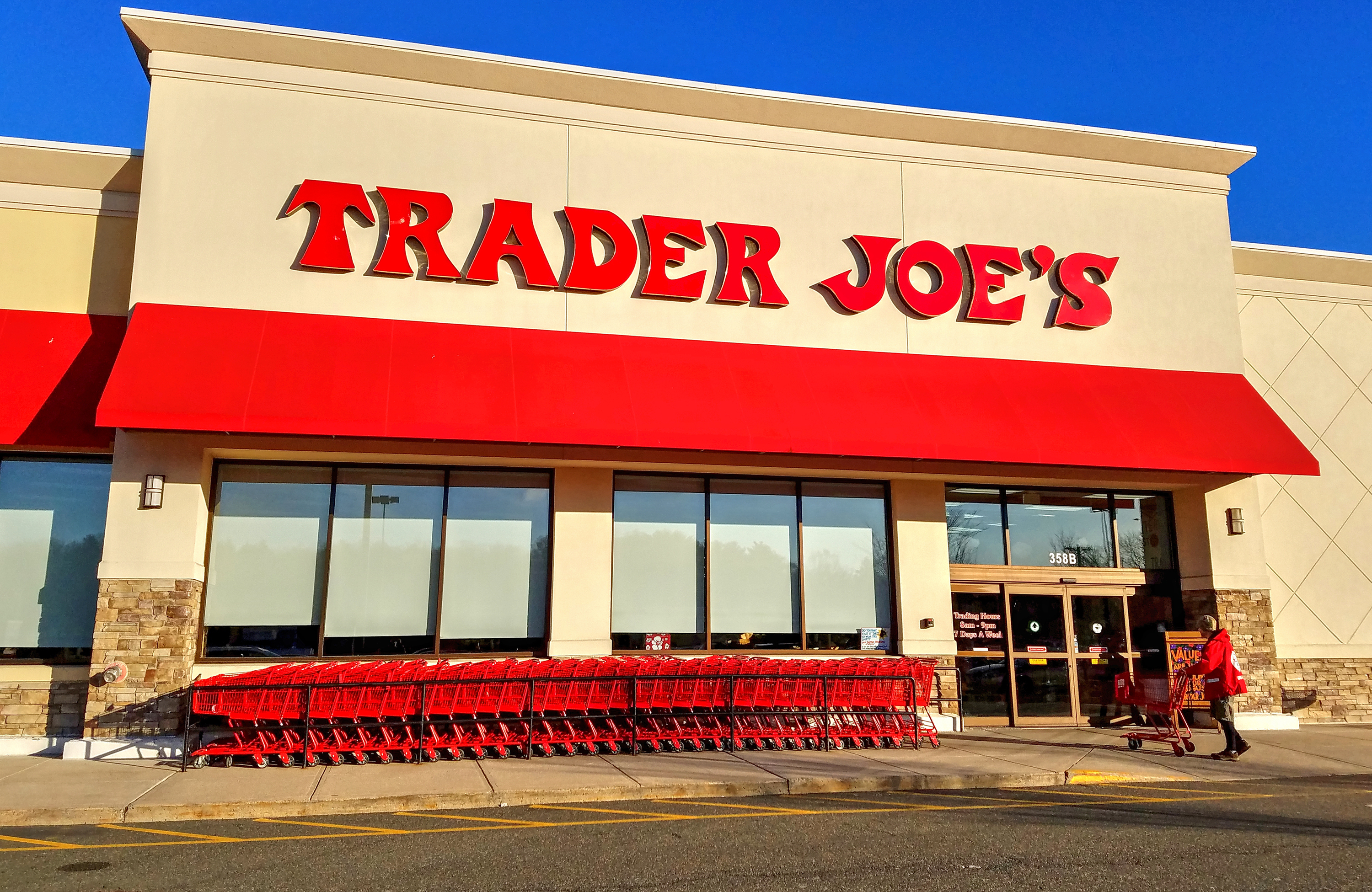 A Trader Joe’s store with red lettering and red awning flanked by red shopping carts. 