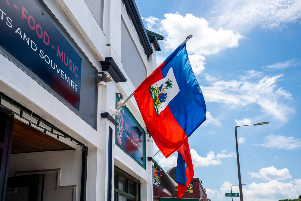 The red and blue Haitian flag flying over a building with white trim on a clear, sunny day.