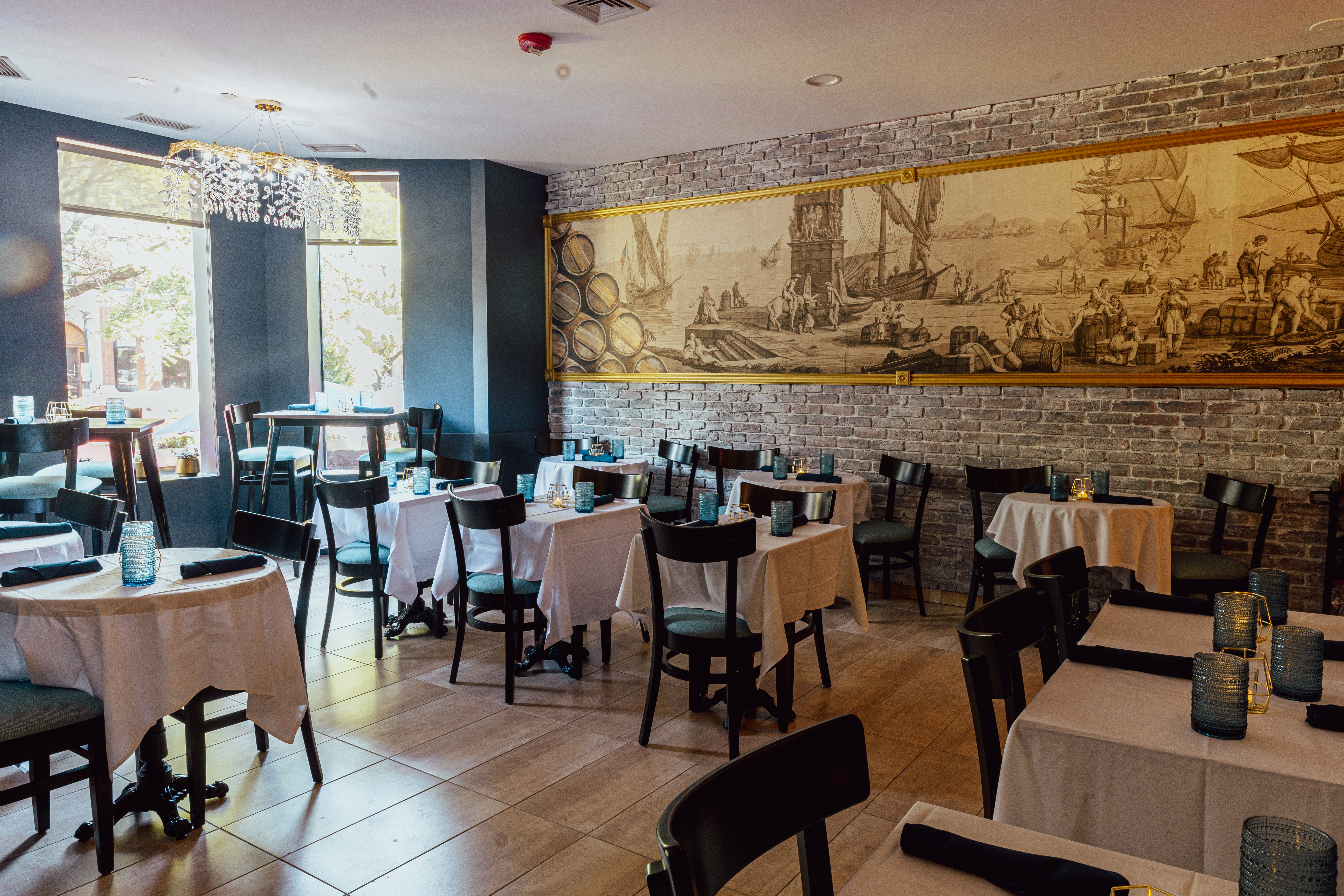 A sunny, empty dining room with white tablecloth-covered tables and chairs.