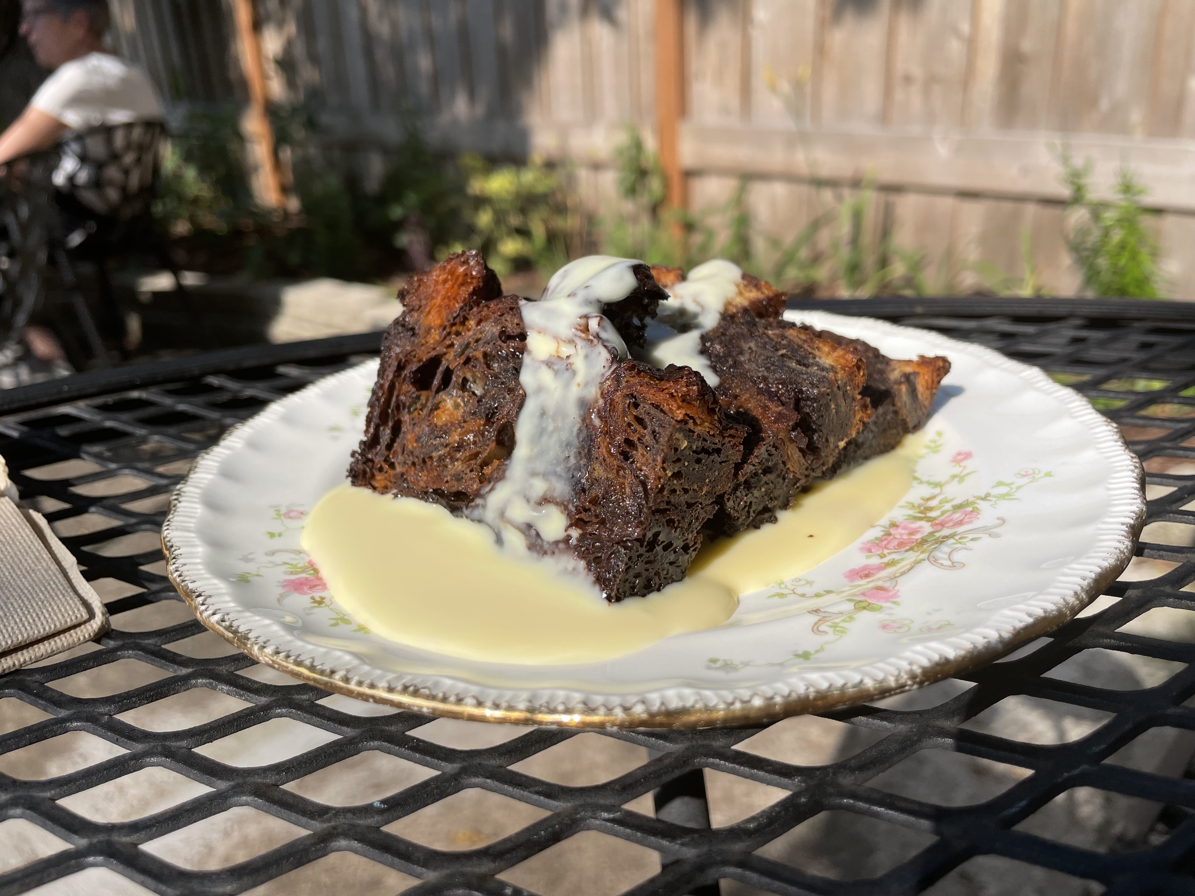 A white floral plate with slices of dark brown bread sitting in a pool of yellow-white creme Anglaise. 