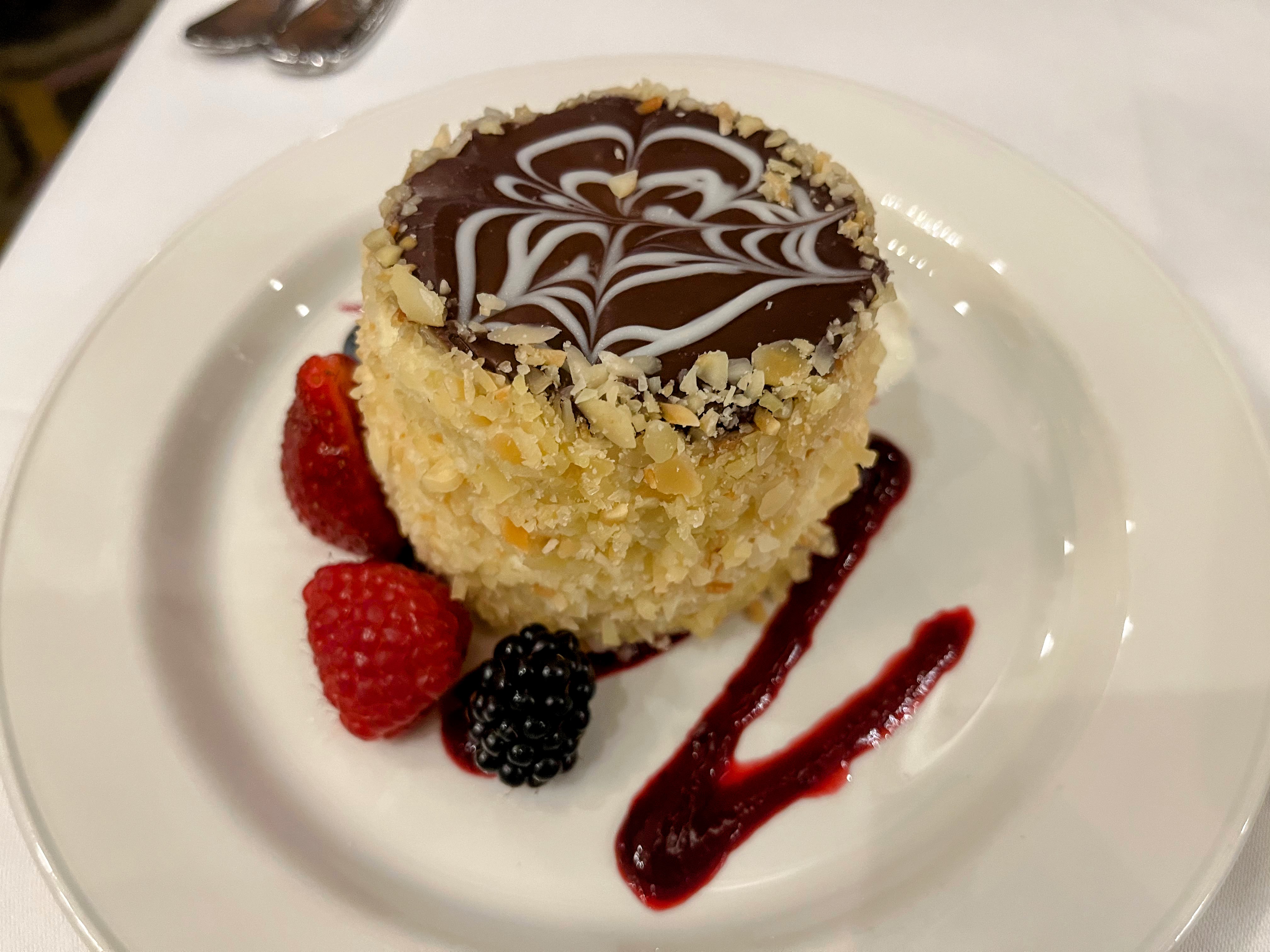 A personal-sized Boston cream pie with berries, whipped cream, and raspberry sauce on the side.