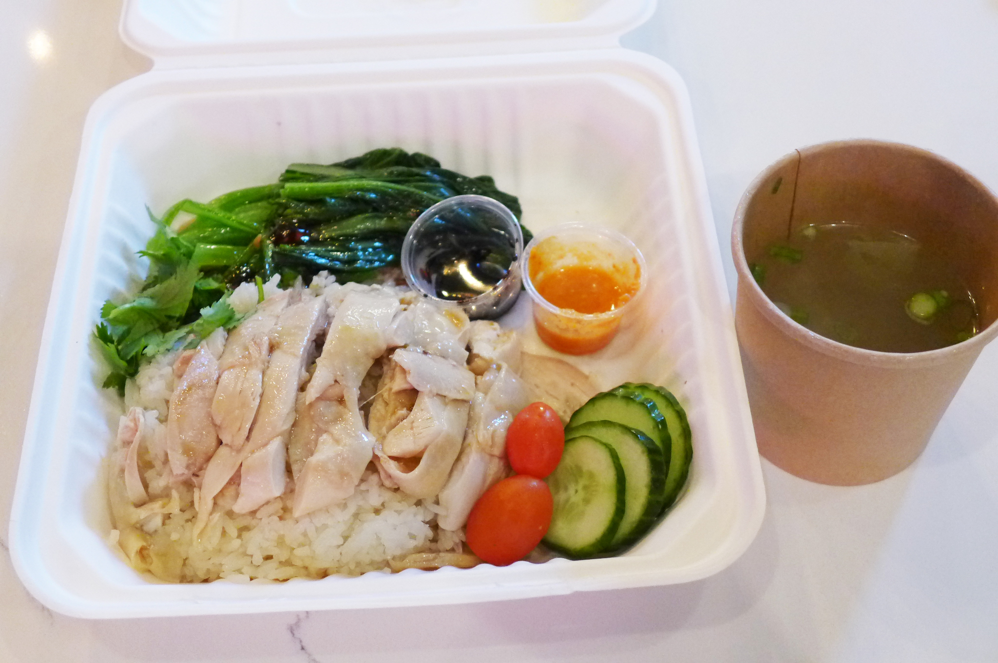 Pale slice chicken on rice served in a white styrofoam container.