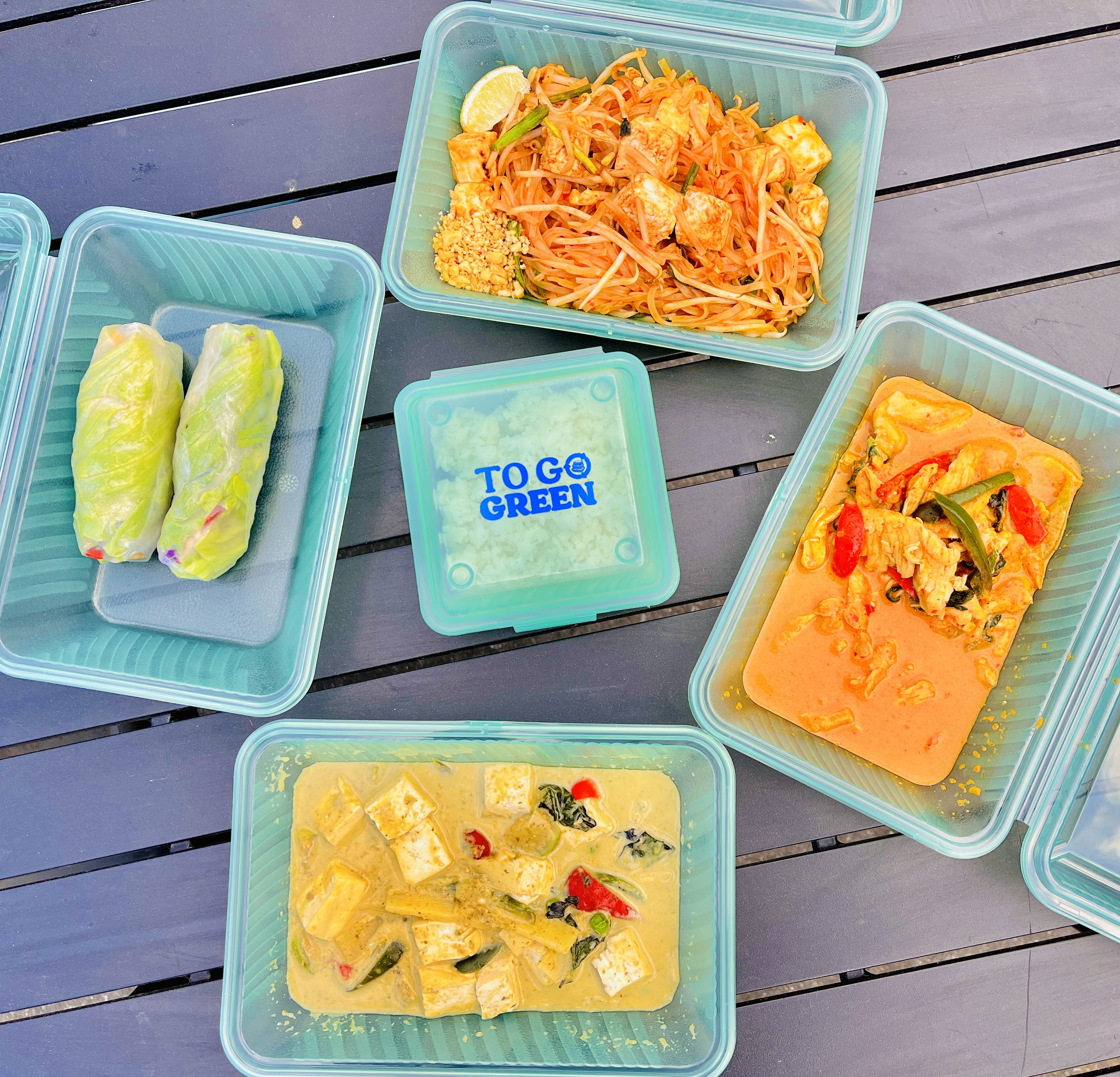 Thai food is seen in bright green reusable plastic containers.