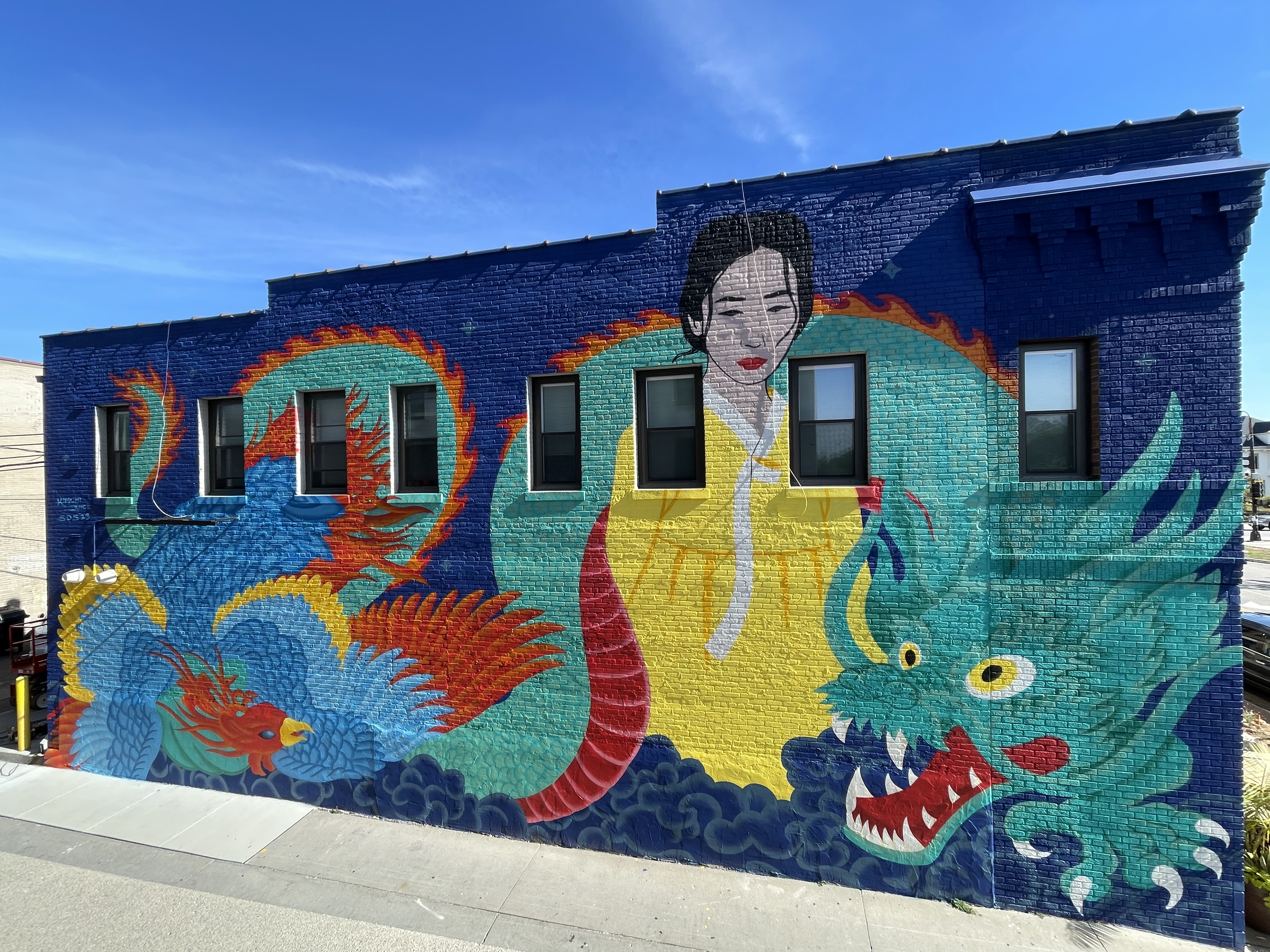 A brightly colored mural of a Korean woman in a yellow hanbok alongside a green dragon and a blue and red phoenix. 