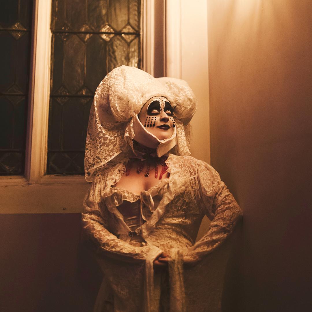 A woman in theatrical makeup and a vaguely gothic outfit.