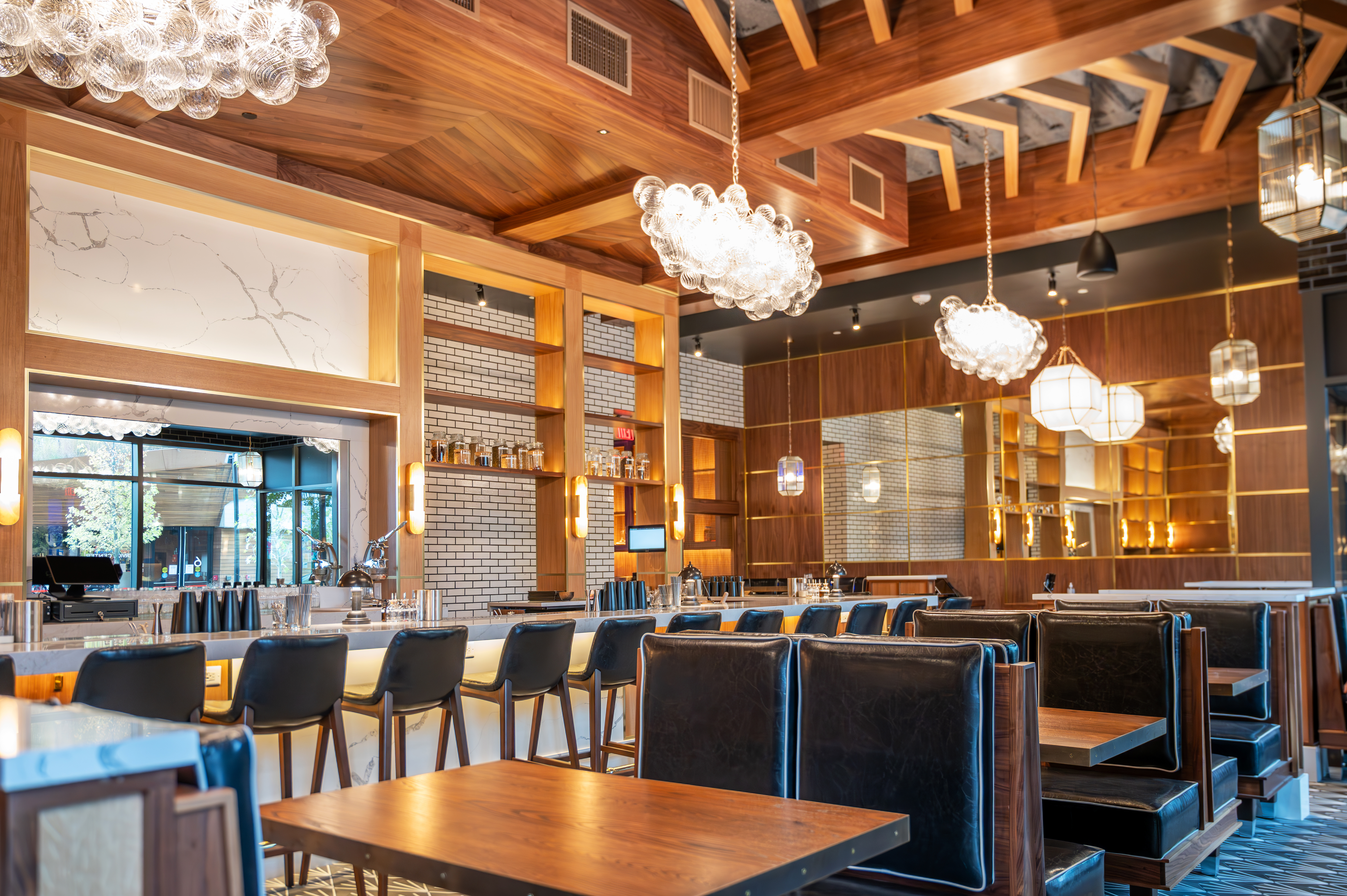 A cocktail bar with high wooden ceilings and booths in the foreground and bar seating in the background.