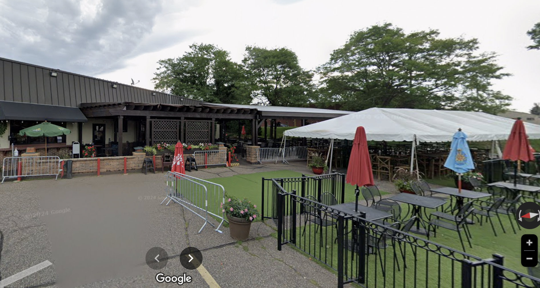 The exterior of a one-story restaurant with a large turf area and patio out front, plus a number of umbrellas and a white tent. 