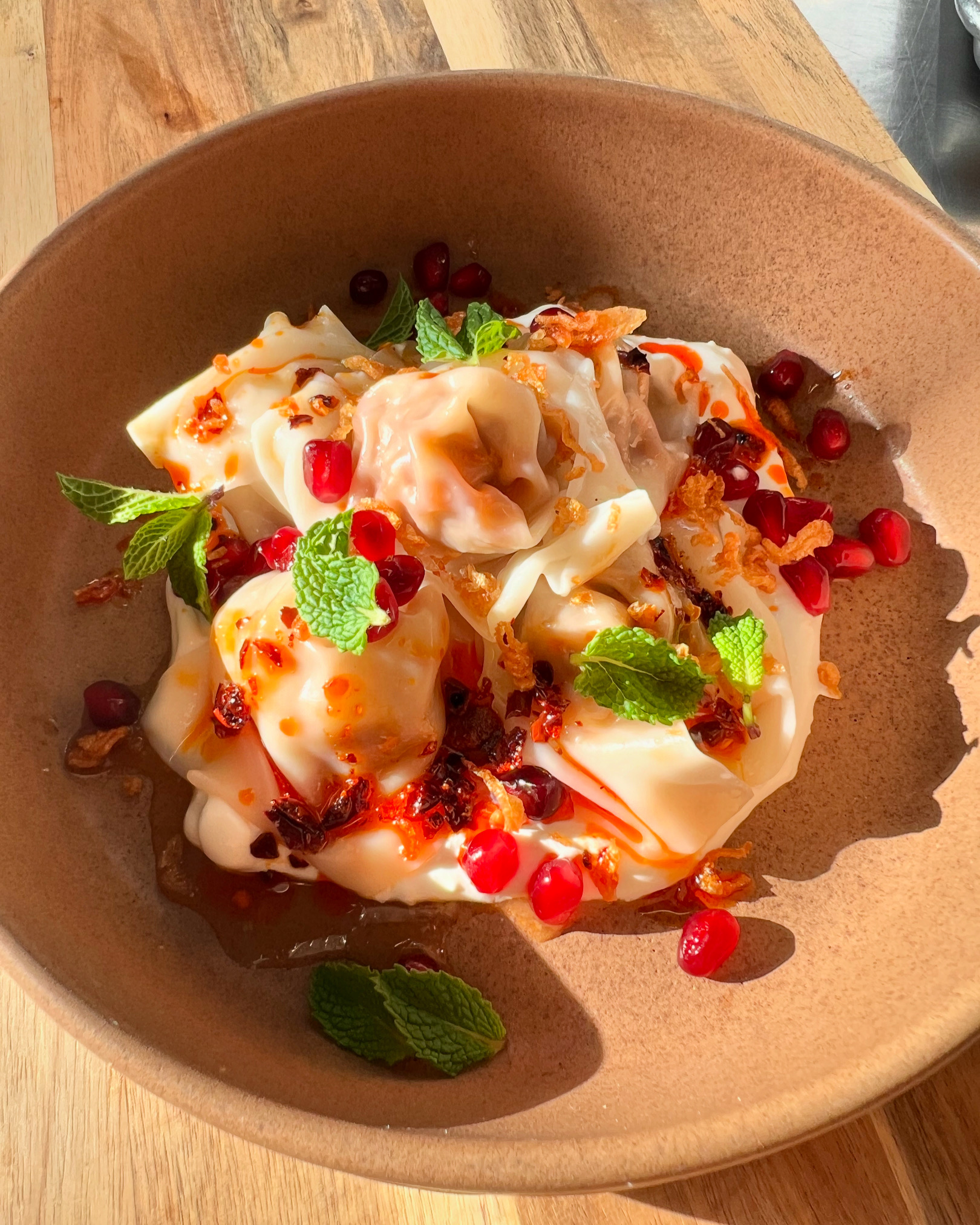 A close-up photo of dumplings garnished with pomegranate and mint in a brown bowl.