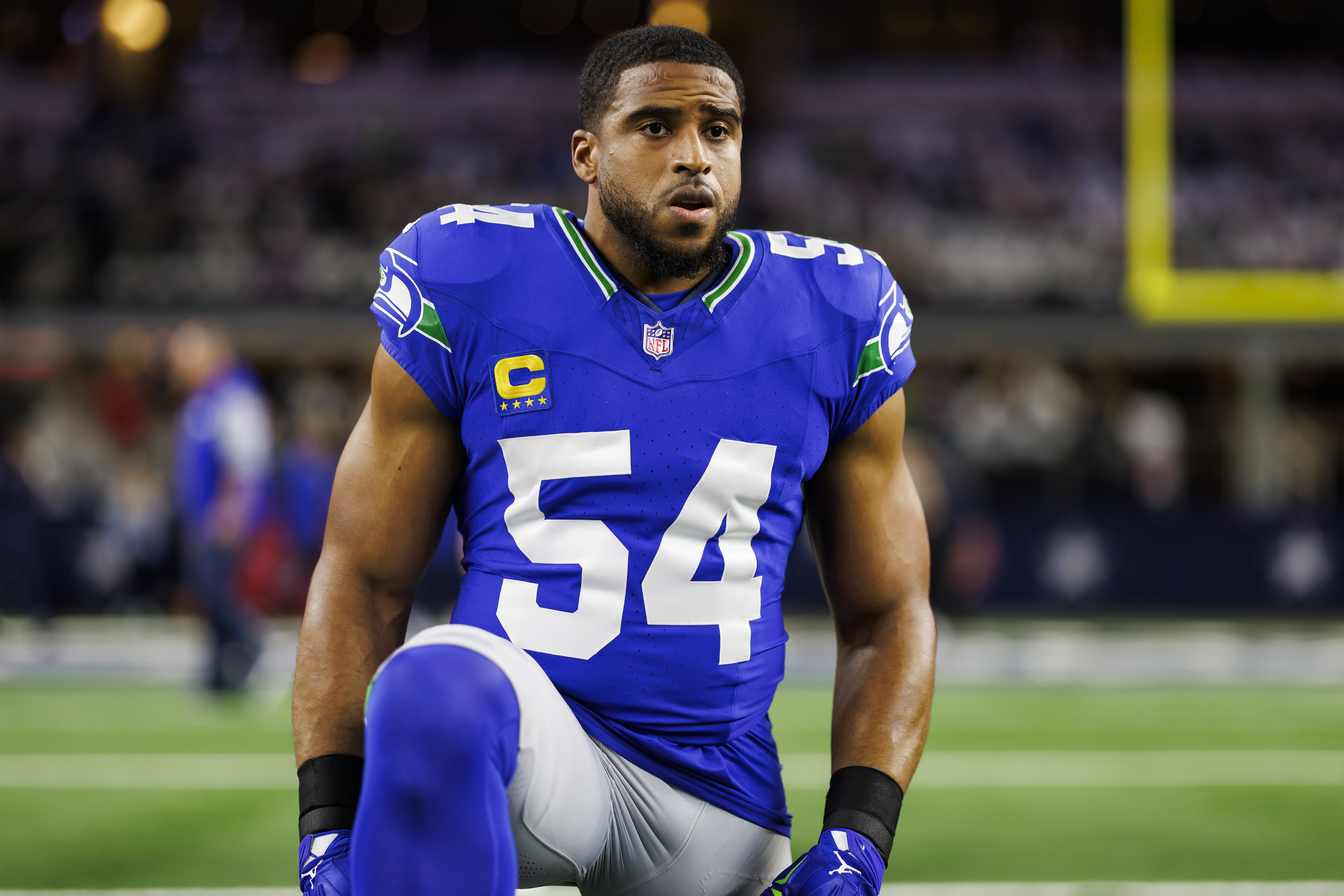 A Black man in a Seahawks uniform kneels on a field.