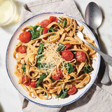 Pasta on a plate with basil and tomatoes.