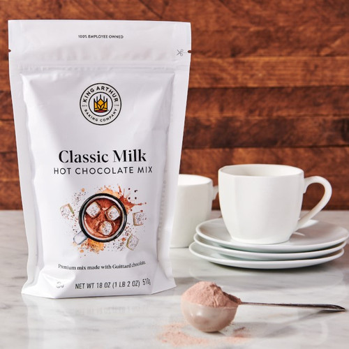 Classic Milk Hot Chocolate Mix package with a scoop of Classic Milk Hot Chocolate Mix and mugs