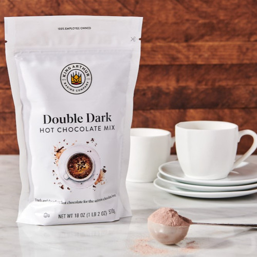 Double Dark Hot Chocolate Mix package with spoonful of mix and mugs.