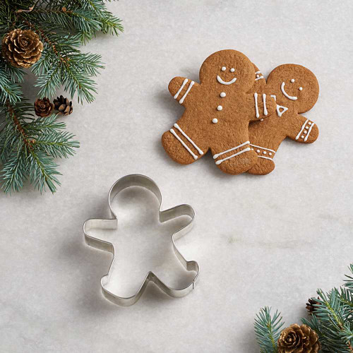 Tin plated gingerbread man cookie cutter next to gingerbread man cookie. Decorated with white cookie icing with buttons and a smile.