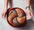 View Red dutch oven with marble rye bread. hands lifting the bread of out the Dutch oven using the white long narrow tabs on the round loaf lifter.