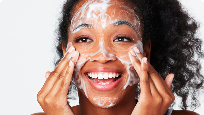 Young woman smiling while massaging foamy cleanser to her face.