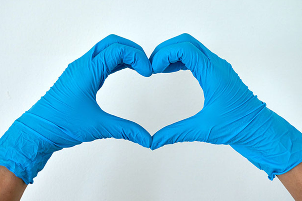 A person wearing blue gloves, with their hands in the shape of a heart