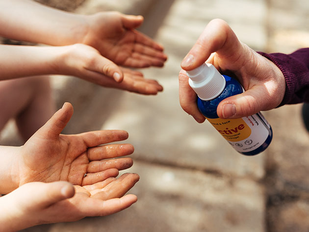 A person applying anti-microbial spray to two sets of hands