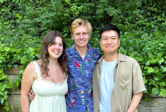 Three students posing in front of green ivy