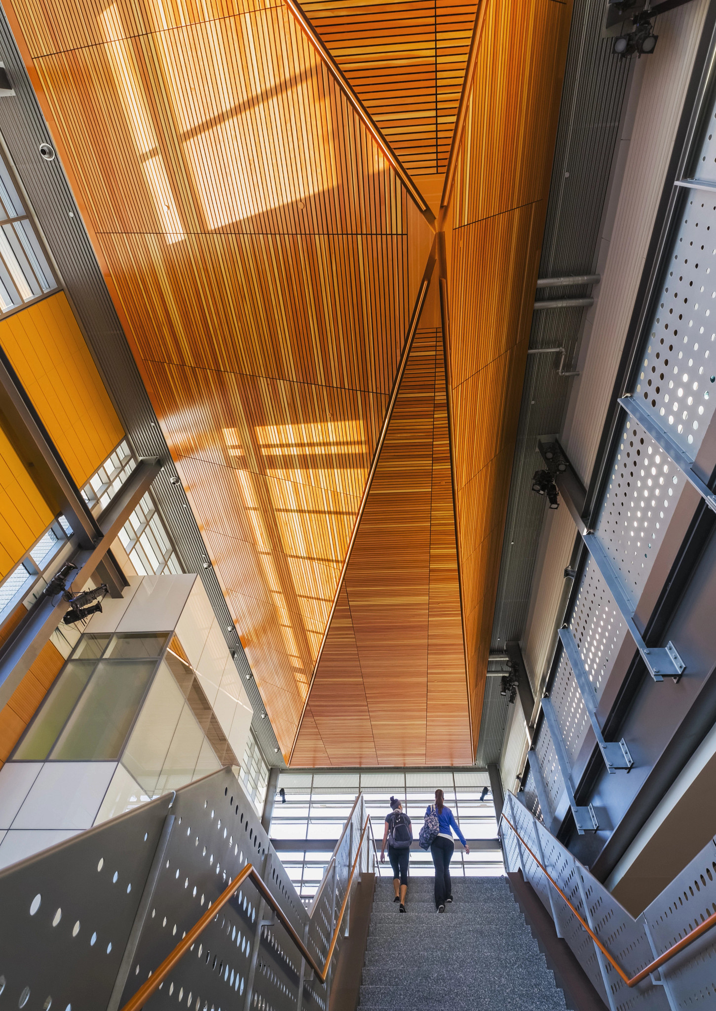 A staircase with two people walking and Wood Panelized Linear ceiling.