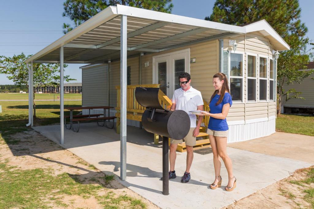 a man and woman standing in front of a barbecue at Red Shoes RV Park and Chalets in Kinder