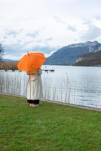 a person with an orange umbrella standing next to a lake at Le Clos Marcel in Duingt