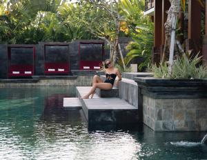 a woman sitting on steps next to a pool of water at La Reserve 1785 Canggu Beach in Canggu