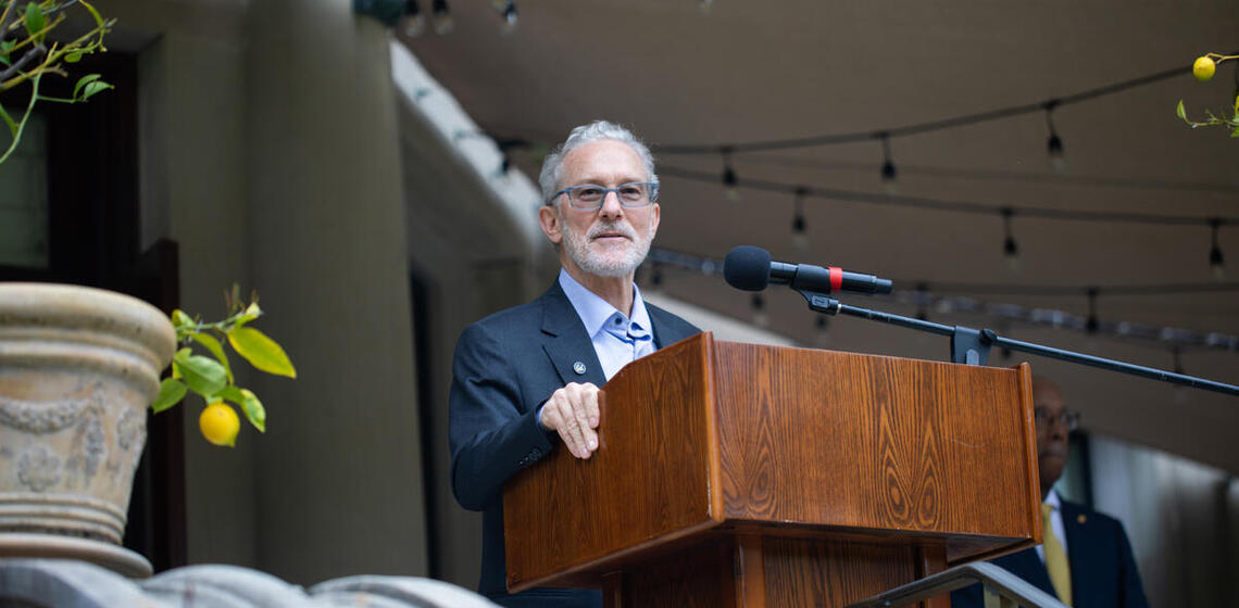 rich lyons speaking at a podium outside of University House