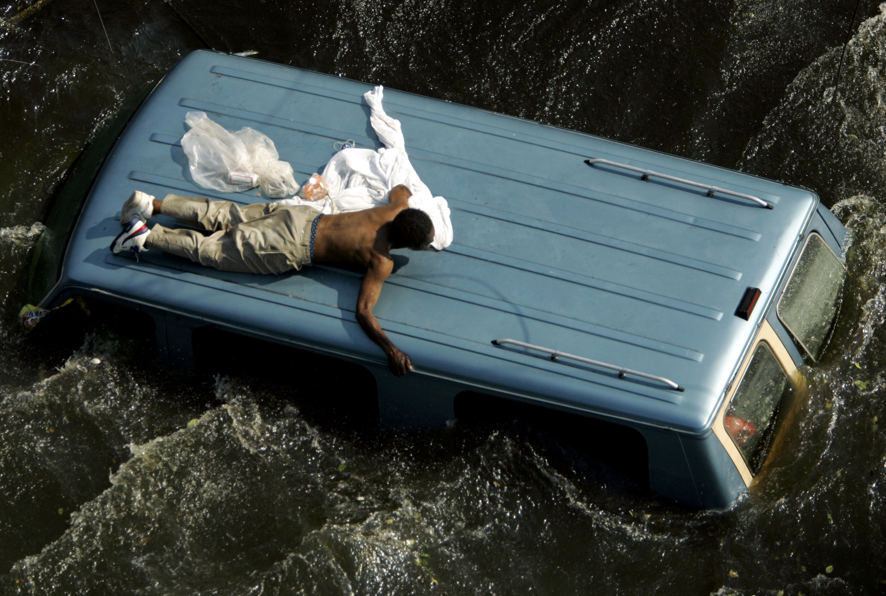 Man clings to top of vehicle in flooded aftermath of Hurricane Katrina in New Orleans.