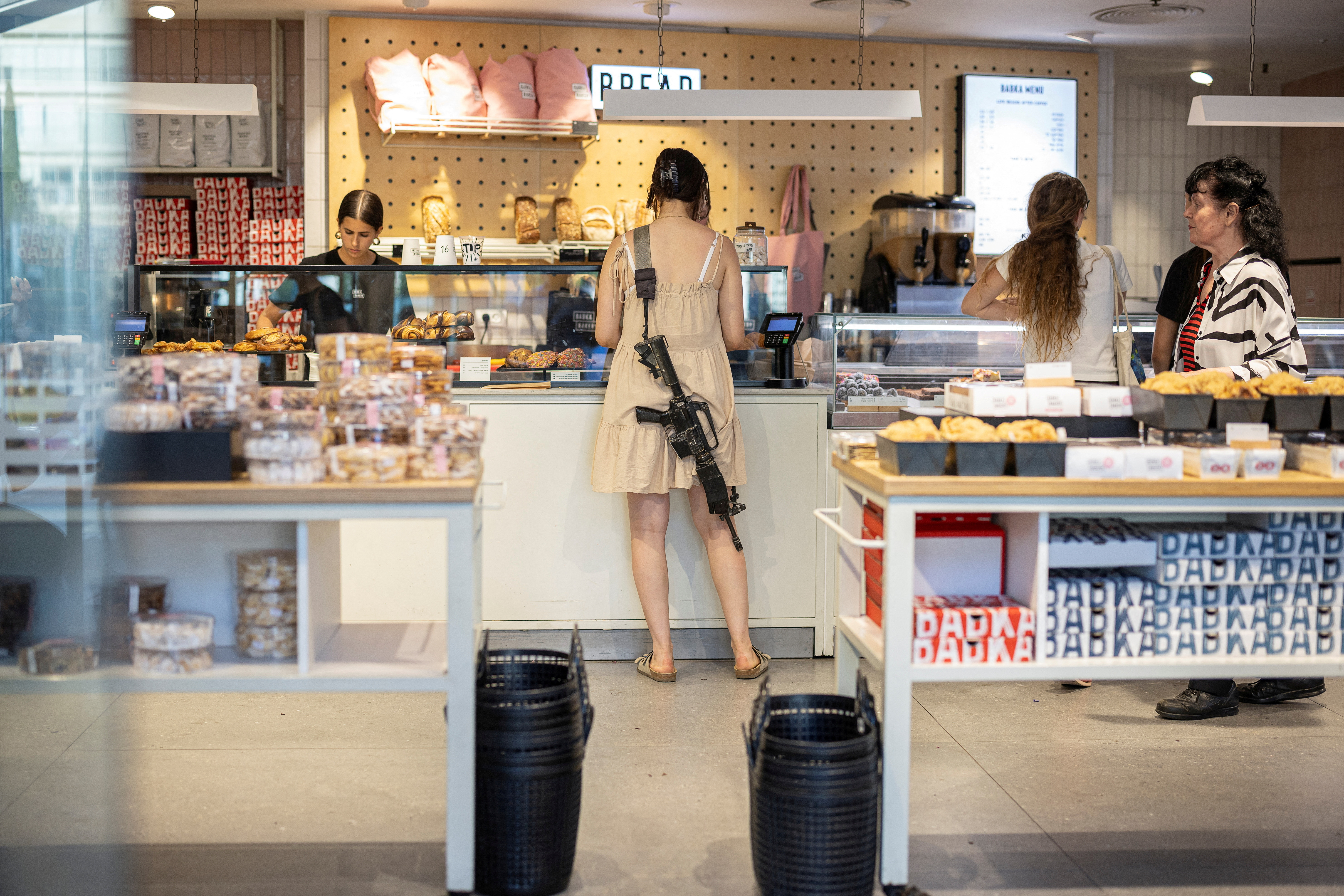 A woman with a rifle shops in a bakery, in Tel Aviv