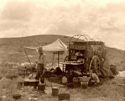 An old photo of a man standing next to a wagon with cowboy recipes.