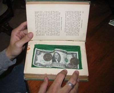 A person holding an open book with a secret compartment for hiding money.