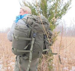 Man carrying a long bag and walking in brush forest.