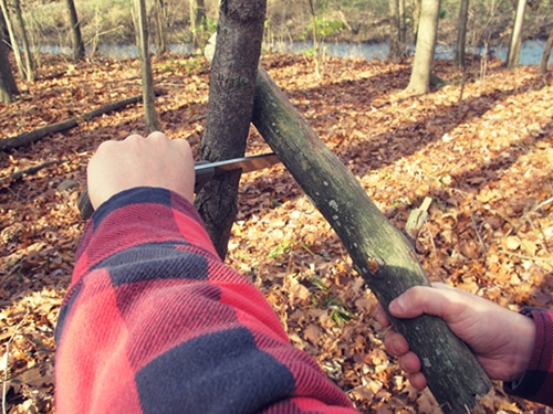 A man using pocket knife for splitting wood.