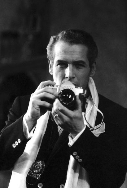 A man in a suit wearing a scarf, capturing a moment with a camera.