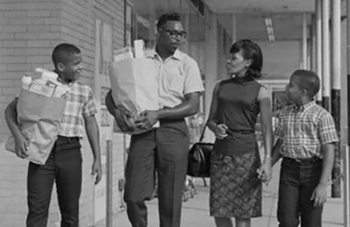 A group of people, with bags in hand, walking down a street.