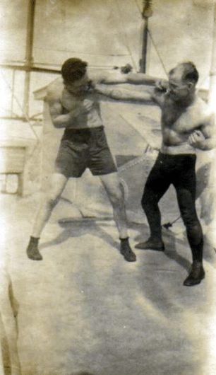 Two men on a boat practicing boxing and taking a punch.