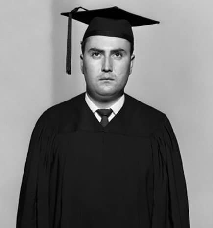 A black and white photo of a man in a graduation gown, representing college graduates and their financial regrets to avoid.