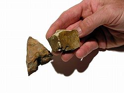 A hand holding a piece of rock, known as flint, and a piece of wood, symbolic of traditional firestarting techniques.