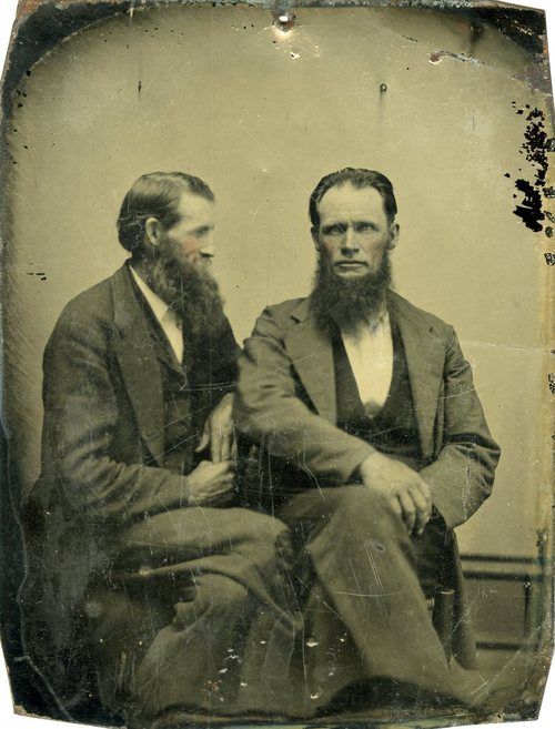 Two men with long beards sitting together wearing suits. 