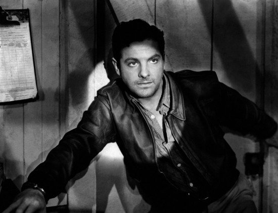 A man in a stylish leather jacket leaning against a wall.