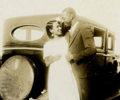 A lasting photograph of a man and woman standing next to a car.