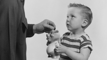 A kid is saving his allowance by putting money into a piggy bank.