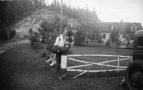 A newly married woman is leaning on a fence in front of a house, offering advice to passersby.