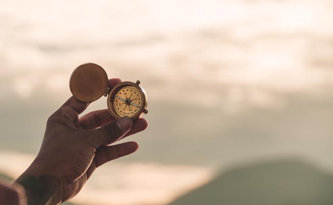 A person finding purpose as they hold a compass in front of a mountain.