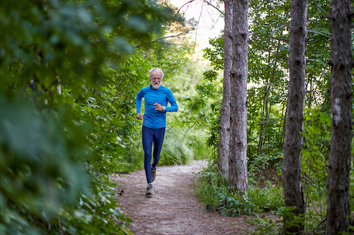 A man is running down a trail in the woods, his movements swift and determined.