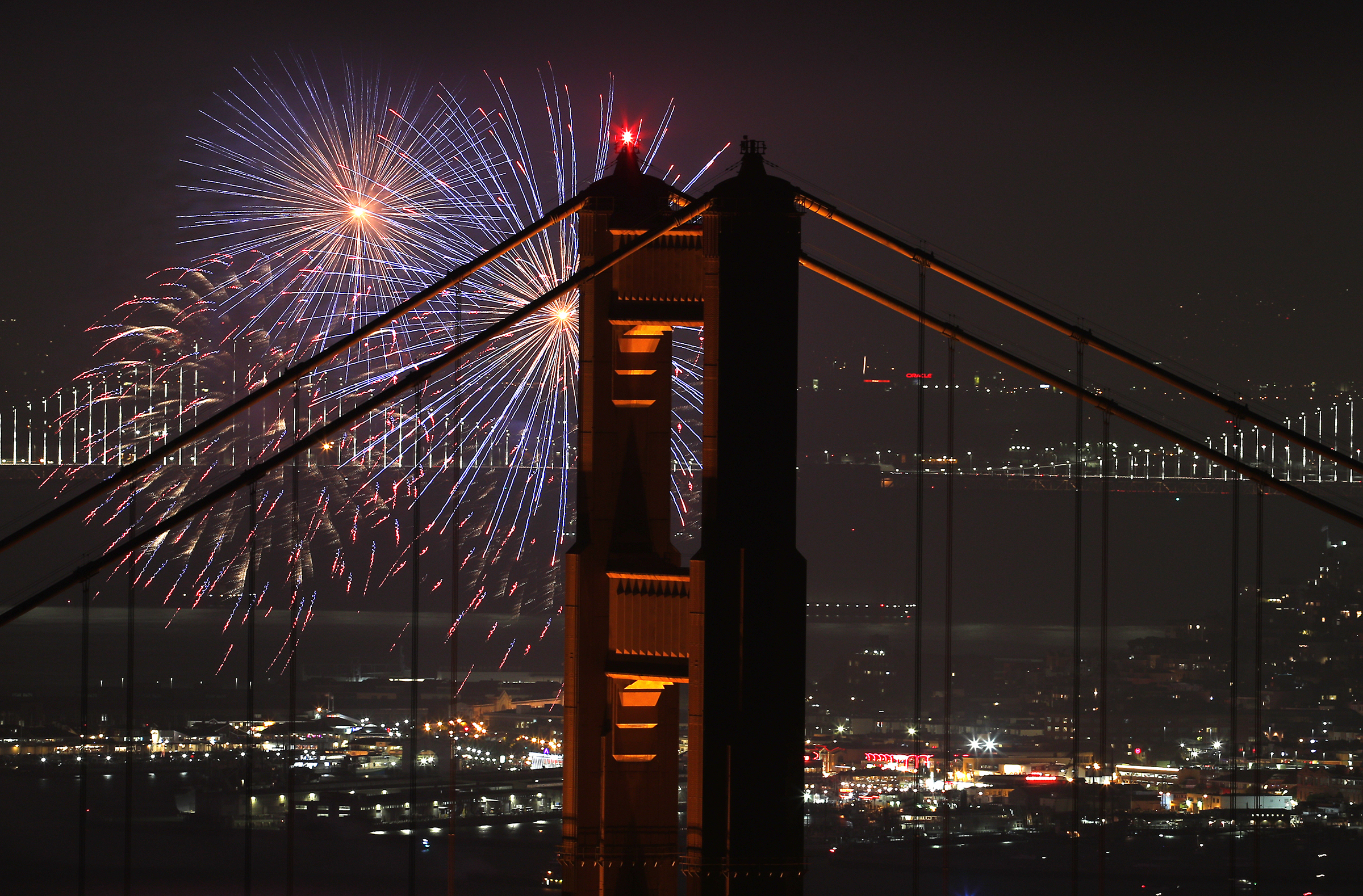 fireworks are shot off in the background of the Golden Gate Bridge.