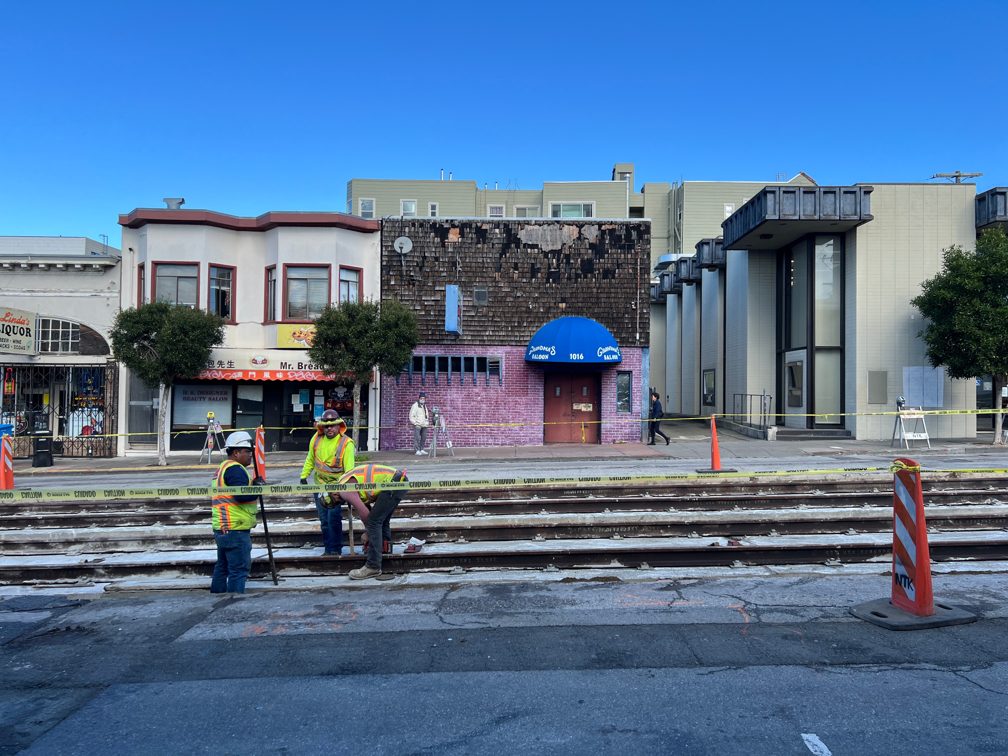 Three construction workers dig out a rail line on a street with caution tape on it.